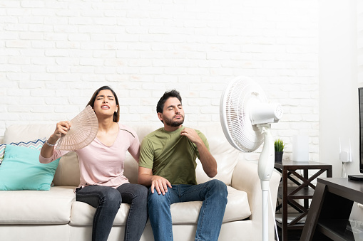 Latin heterosexual couple feeling hot while sitting in front of fan at home