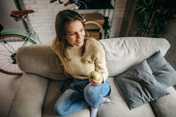 istock Young women sitting on sofa and eating apple 1213582803