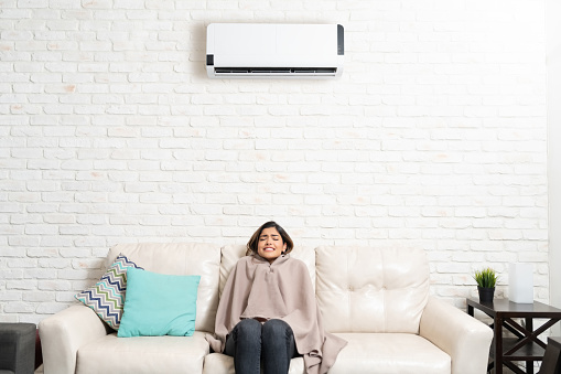 Hispanic young woman feeling cold while sitting on sofa in living room at home with air conditioning