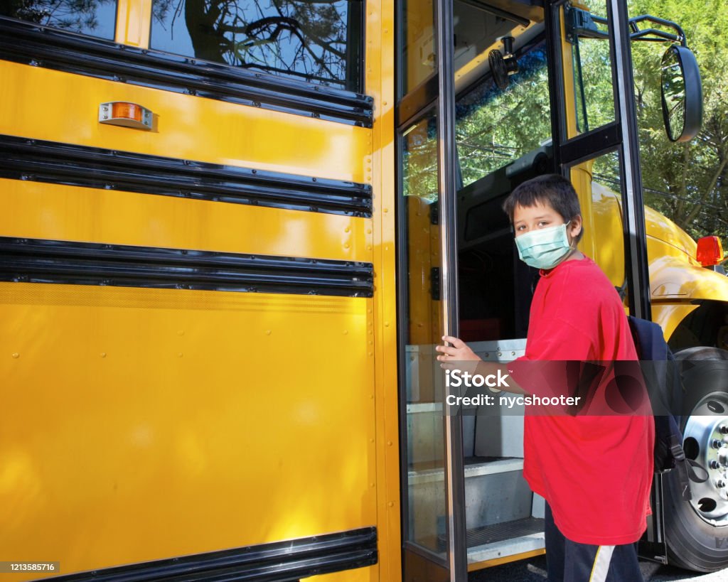 school age boy wearing surgical mask Young elementary school boy climbs on to school bus wearing surgical mask School Bus Stock Photo