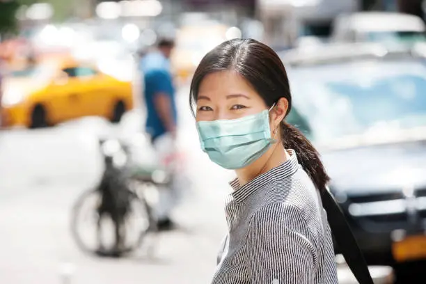 Young Asian woman wearing a surgical mask crossing the streets of New York City