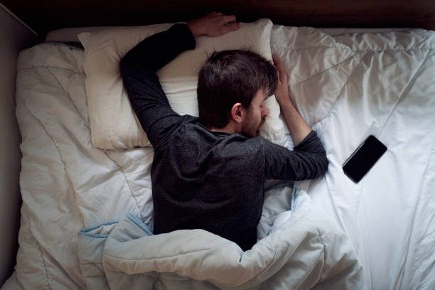 Young male sleeping in the bed only himself during the day smartphone next to him stock photo