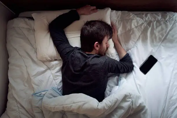 Photo of Young male sleeping in the bed only himself during the day smartphone next to him