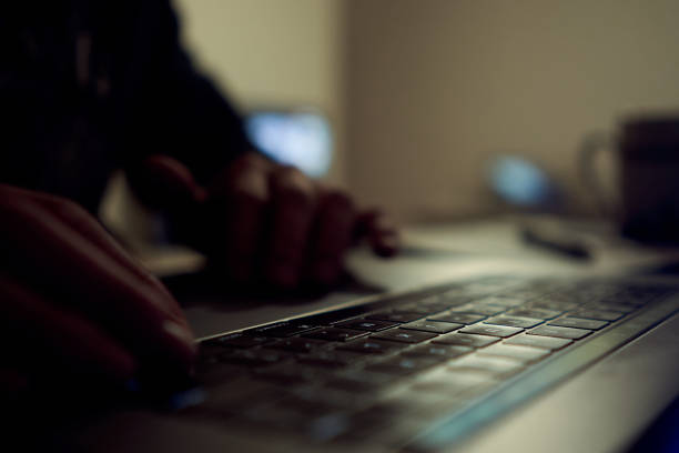 a laptop computer at the morning with sunshine backlight in a dark room with blank white screen shot with focusing on finger and keyboards and keep other part fo photo blurred