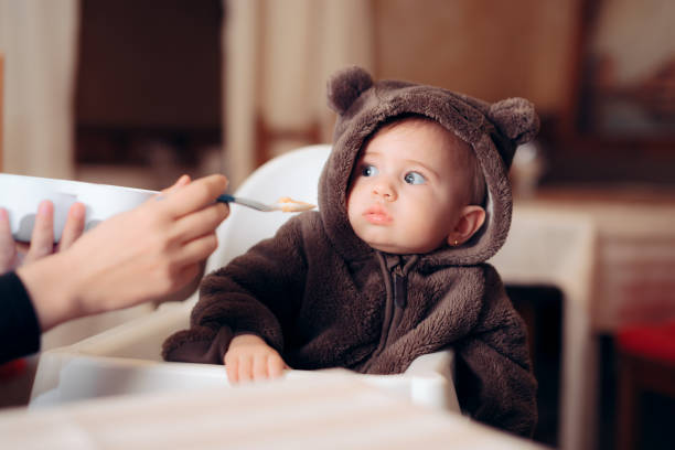 bebé divertido sentado en trona negándose a comer - baby food fotografías e imágenes de stock