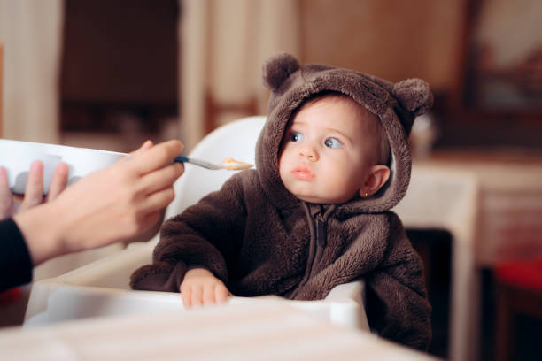 Funny Baby Sitting in Highchair Refusing to Eat Small infant being a picky eater disliking the food refusing photos stock pictures, royalty-free photos & images