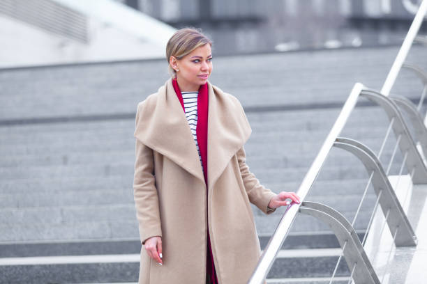 at the mall lifestyle fashion portrait of stunning brunette girl. walking on at the mall. going shopping. wearing stylish white fitted coat, red neckscarf. business woman. black bag - neckscarf imagens e fotografias de stock