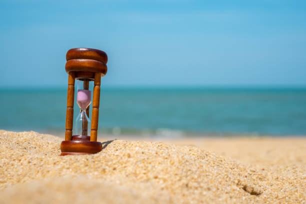 istock Small hourglass show time is flowing on sand beach texture background. 1213602072