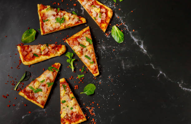 istock Cut into slices hawaiian pizza with ham and pineapple on a dark background. Top view. 1213608146