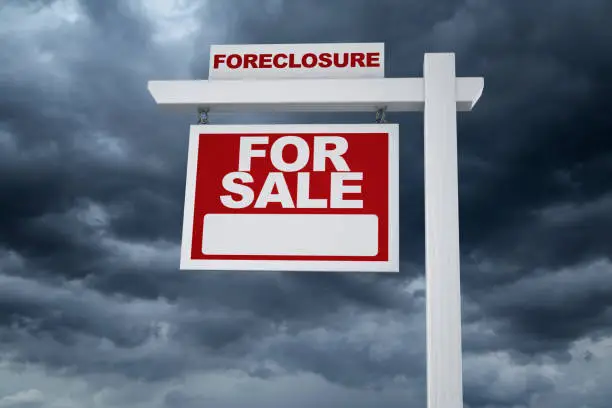 Real Estate Market Crash - Real estate sign and with the word foreclosure and dark ominous clouds in neighborhood.