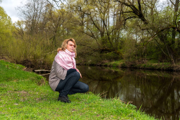 istock Pensive woman squatting by the river. 1213625101