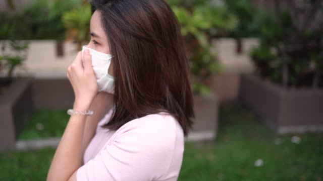 4K Asian young lady talking on the phone wearing white mask, coughing and sneezing, air pollution, virus covid19, respiratory disease, outside resident building, smart life self quarantine, order food