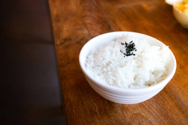 arroz en una taza blanca sobre fondo de madera y sésamo negro - sesame black stack cereal plant fotografías e imágenes de stock