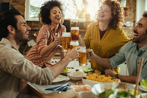 Group of young cheerful people toasting with friends and having fun while having lunch together at home. Focus is on redhead woman.