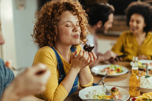 This is so delicious! Young woman with eyes closed enjoying in taste of food while eating with friends at dining table. dessert sweet food stock pictures, royalty-free photos & images