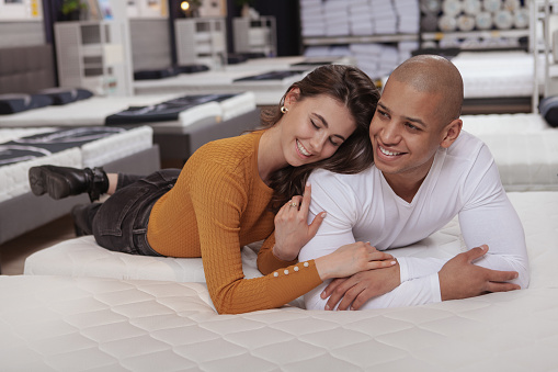 Happy multiethnic couple laughing, enjoying shopping together for a new bed for their new home