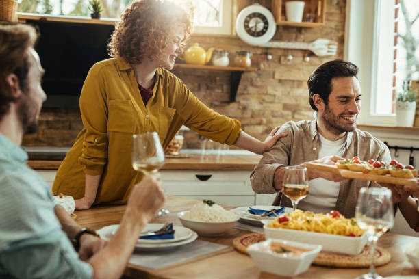 istock Happy friends talking and having fun while passing food at dining table. 1213636851