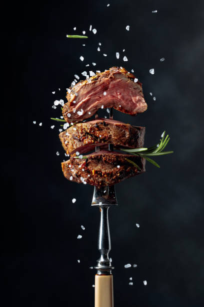 Grilled ribeye beef steak with rosemary and salt. Grilled beef steak with spices on a black background. Beef steak on a fork sprinkled with rosemary and sea salt. fork photos stock pictures, royalty-free photos & images