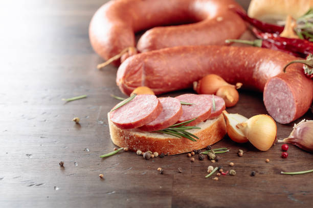 Sandwich with salami. On a old wooden table sausage with bread, rosemary, onion, garlic and pepper.