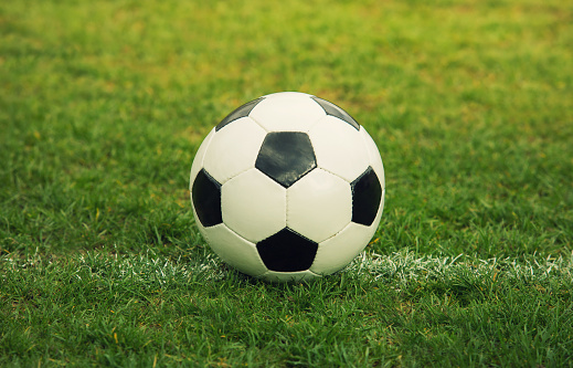 Classic soccer ball, typical black and white hexagon pattern, placed on the stadium turf. Traditional football ball on the green grass field of arena.