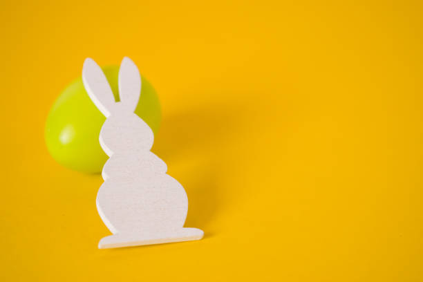 istock White Easter bunny and green egg on yellow background. Easter holiday background 1213641807