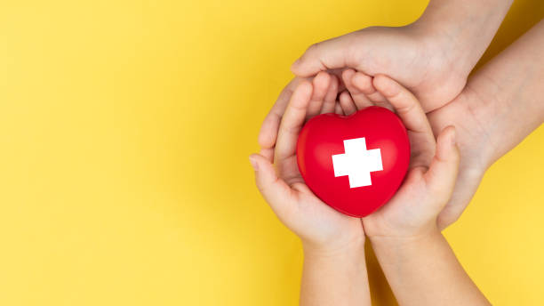 world red cross day, adult and child hands holding red heart, healthcare, love and family insurance concept stock photo