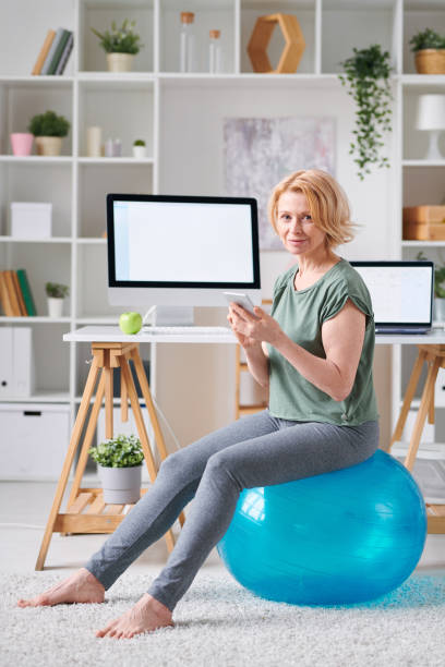 femmina piuttosto matura con smartphone alla ricerca di un corso di fitness online - yoga business women living room foto e immagini stock