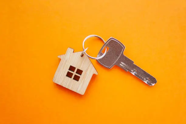 Key and house shaped keychain arrangement on orange background. Top view, flat lay. Real estate, insurance concept, mortgage, buy sell house, Real Estate Agent concept