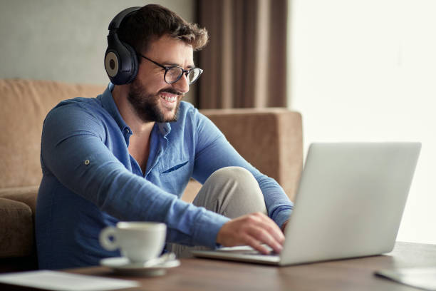 istock Smiling man with headphones using laptop in his home 1213655435