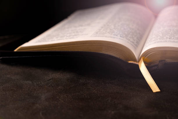 istock Open Bible on a dark table with light coming from above. Christianity concept. Holy Bible background. 1213655749