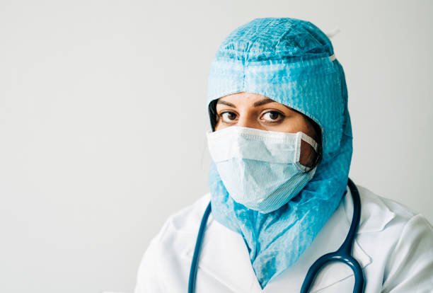 Female Doctor Wearing Surgical Cap And Mask Working Against Blue Background