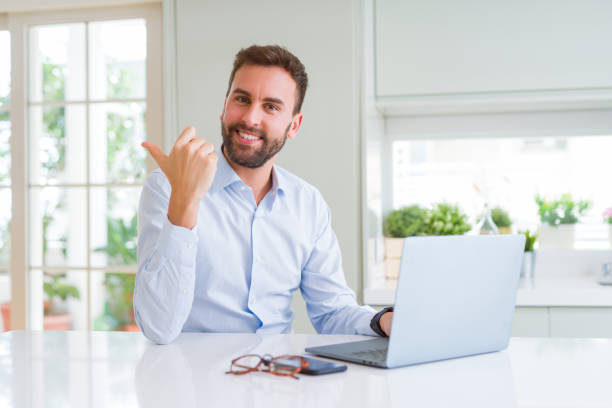 istock Handsome business man working using computer laptop pointing and showing with thumb up to the side with happy face smiling 1213664396