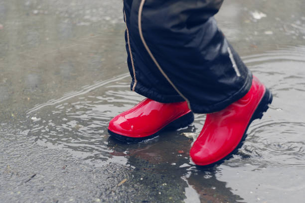 istock A small baby plays merrily in the spring in a puddle, splashing with a stick. Rubber boots. 1213666446