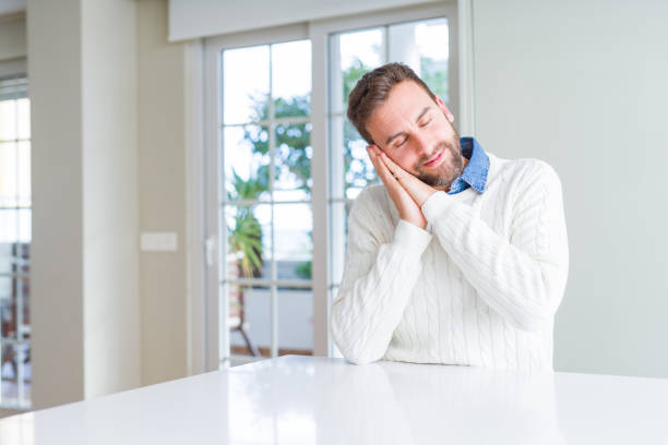istock Handsome man wearing casual sweater sleeping tired dreaming and posing with hands together while smiling with closed eyes. 1213666542