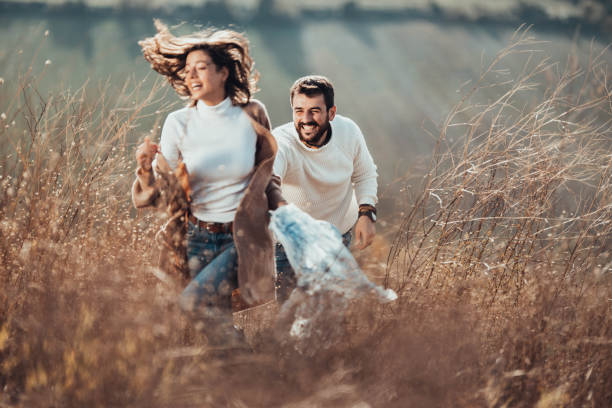 giovane coppia felice che insegue l'erba alta su una collina. - chasing women men couple foto e immagini stock