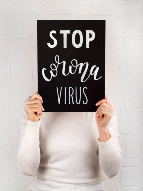 Woman keeps in hands a black chalkboard with inscription STOP CORONAVIRUS Woman keeps in hands a black chalkboard with inscription STOP CORONAVIRUS the human body writing black human hand stock pictures, royalty-free photos & images