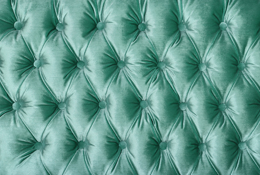 Pastel teal green velvet capitone textile background, retro Chesterfield style checkered soft tufted fabric furniture diamond pattern decoration with buttons, close up