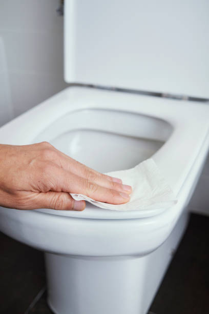man cleaning the toilet seat with a piece of paper closeup of a caucasian man cleaning the toilet seat with a piece of toilet paper in a tiled bathroom Phobia stock pictures, royalty-free photos & images