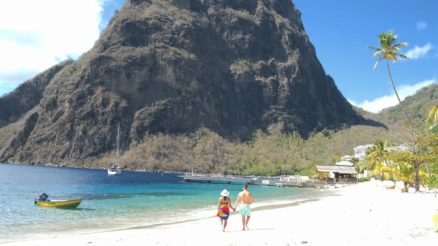 Huge pitons drone view at Saint Lucia sugar beach St Lucia mountains, couple men and woman waling at the white sugar beach during vacation