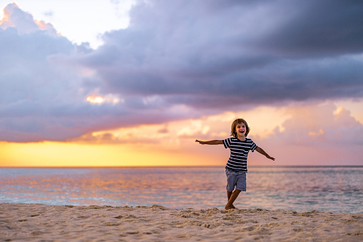 Happy little boy having fun while spinning with his arms outstretched on the beach at sunset. Copy space.