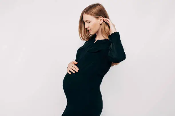Photo of Pregnant happy woman in black dress. Fashion shot in the studio on a white background. Beautiful pregnant girl