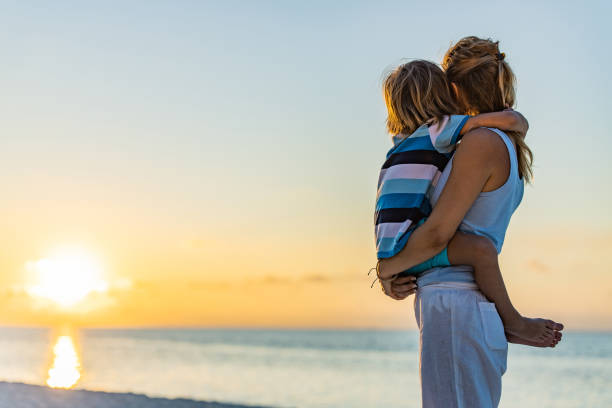 Loving single mother and son looking at sunset view from a beach.