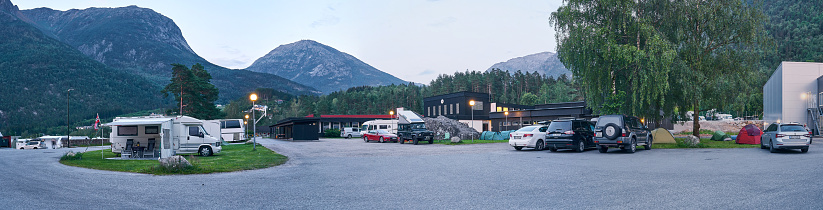 Norway - July 13, 2019: Panorama of camping in Norway. tourist houses, campers, trailers and cars are in the parking lot, tents are located nearby. In the background mountains are visible, evening comes