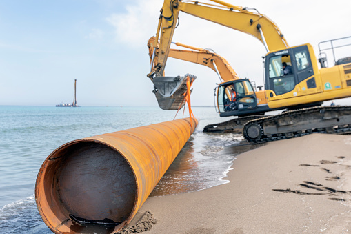 The excavators are transporting pipe piles for offshore piling construction. In drilled pier foundations, the piers can be connected with grade beams on which the structure sits.
