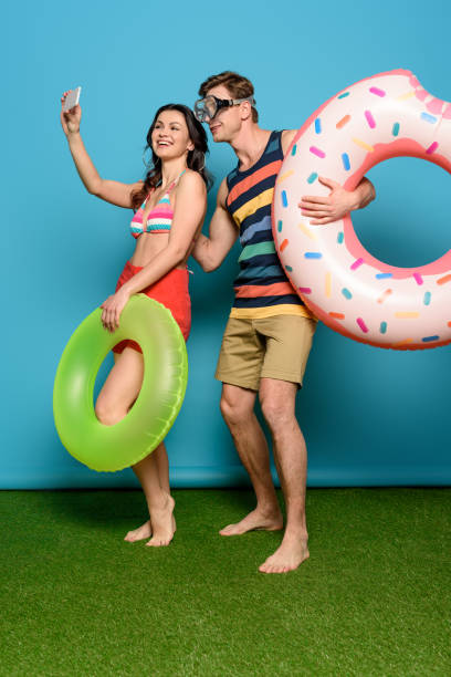 istock cheerful couple with inflatable rings taking selfie on smartphone on blue background 1213687365