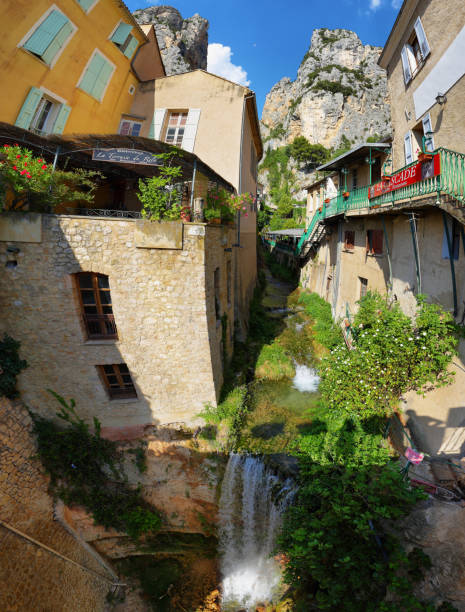 Tourists in the narrow street of thel medieval village Moustiers Sainte Marie, France" Moustiers Sainte Marie, France - Jul 4, 2019: houses and waterfall Tourists in the narrow street of the medieval village Moustiers Sainte Marie. Village is included in list of "The most beautiful villages of France" sainte marie stock pictures, royalty-free photos & images