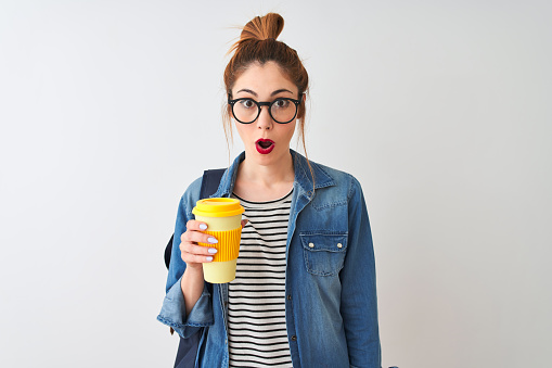 Beautiful redhead student woman drinking take away coffee over isolated white background scared in shock with a surprise face, afraid and excited with fear expression