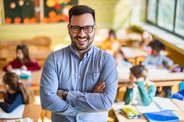 istock Happy elementary teacher with crossed arms in the classroom. 1213691391