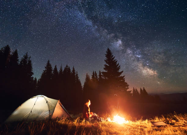 istock Woman enjoying starry night sky near campfire. 1213691565