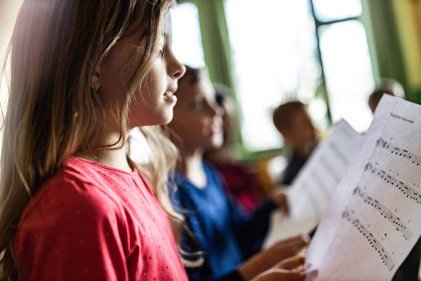 Schoolgirl practicing with sheet music on a class at school. Elementary student reading musical notes on a music class at school. school choir stock pictures, royalty-free photos & images
